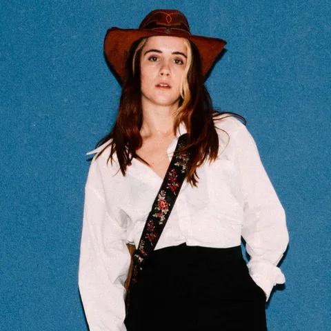 Rae Isla in a cowboy hat against a blue wall