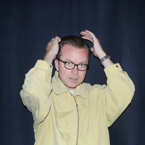 Tom Vek in a yellow jacket, hands on his head